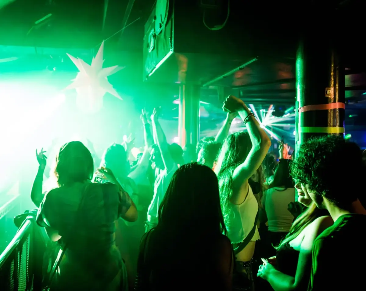 A crowd in green light at a Glitterbomb day party